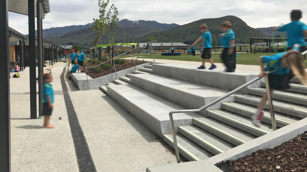 Children using concrete terraced seating, steps and landscaped play areas at Shotover Primary School.