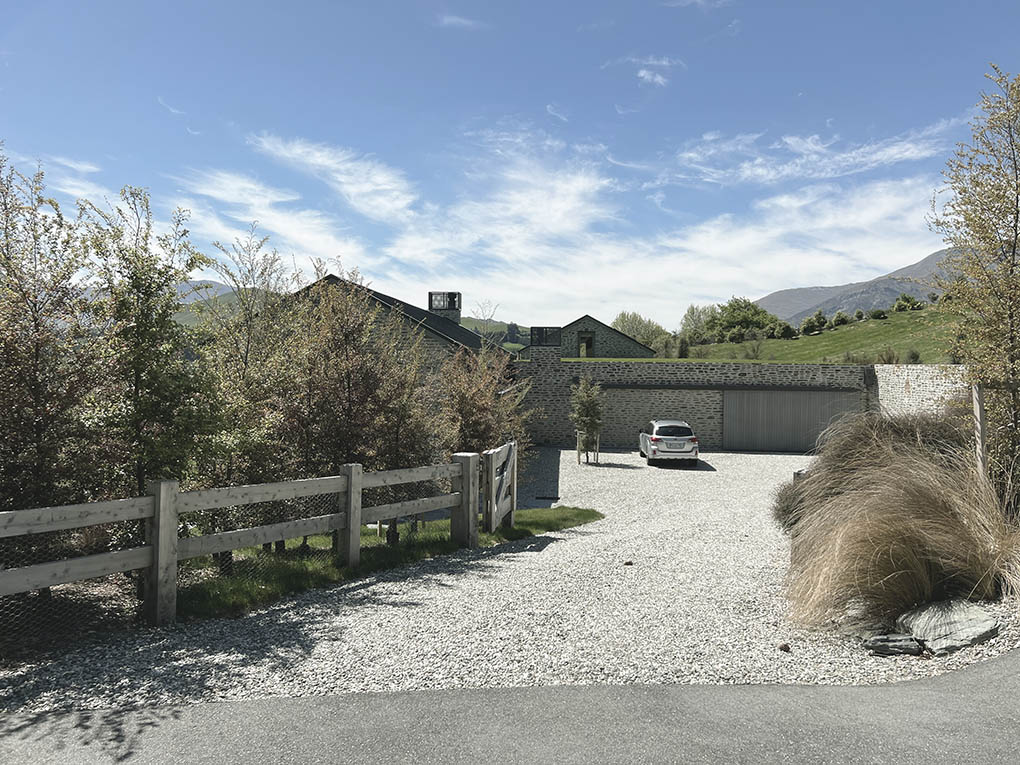 Gravel driveway and timber entry gate at Shotover River House, framed by tussocks and mountain beech trees.