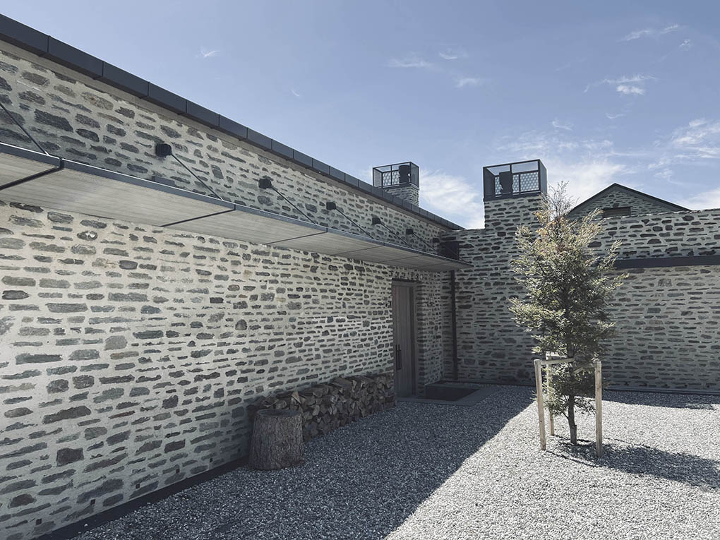 Enclosed gravel courtyard at Shotover River House framed by schist walls and a specimen beech tree.