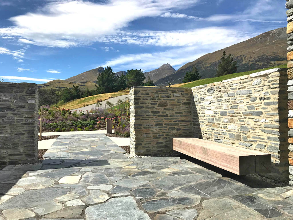 Schist-walled entry courtyard at Blanket Bay Villas with flagstone paving and a timber bench.