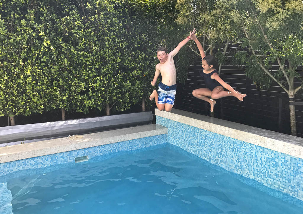 Children jumping into the Freemans Bay swimming pool beside a timber privacy screen and bench.