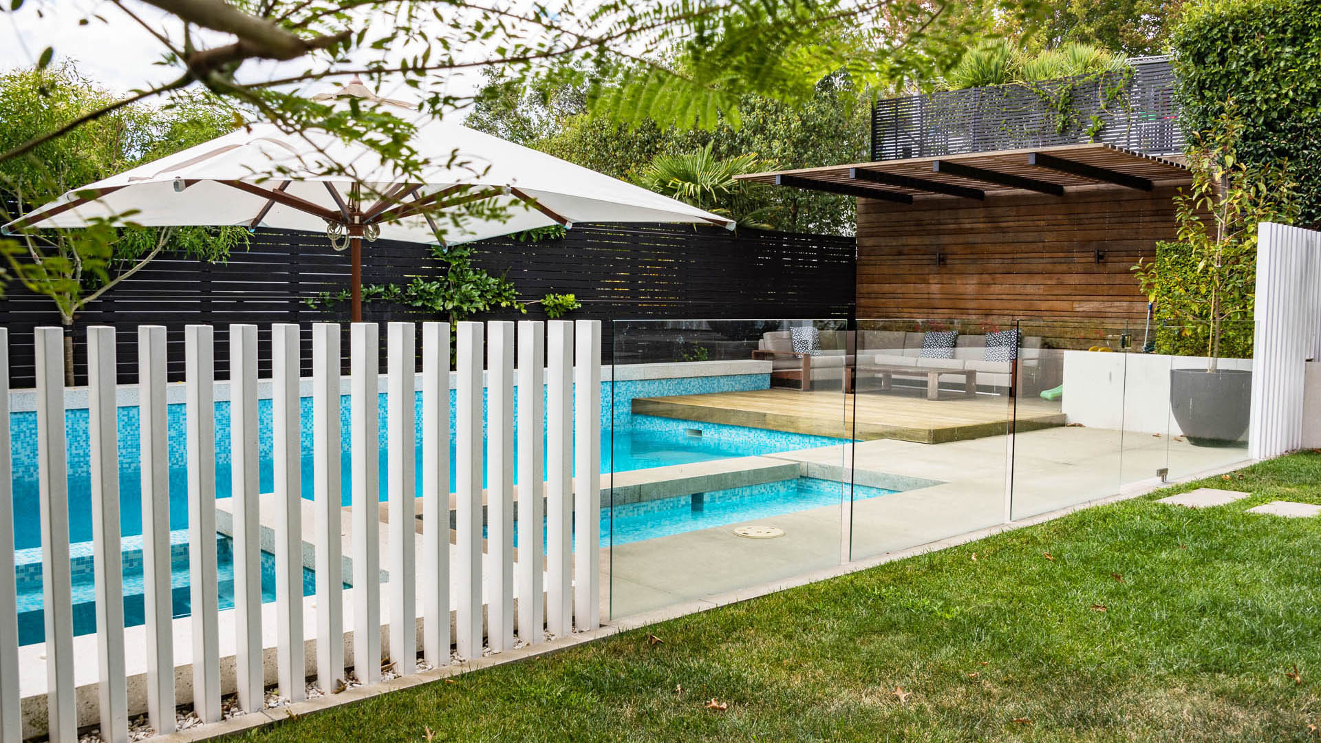 Freemans Bay garden with a swimming pool, raised spa, glass fence, lawn and timber cabana.