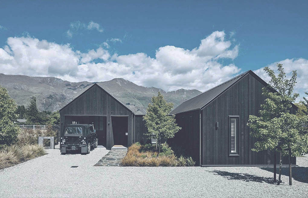 Gravel drive and native planting around Wānaka Barn House with mountain views beyond.