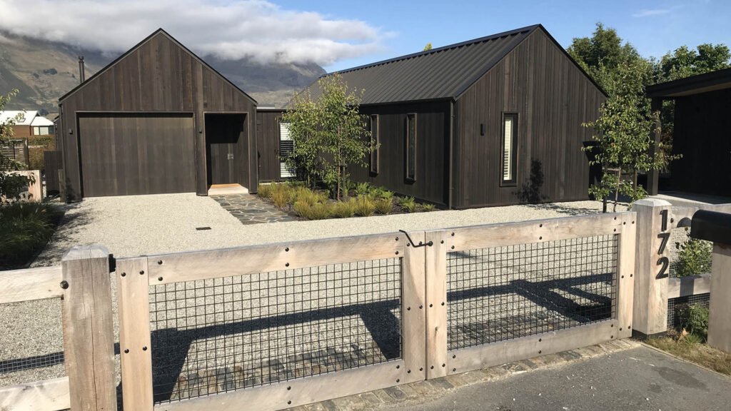 Timber entrance gates, gravel drive and planted front garden at Wānaka Barn House.