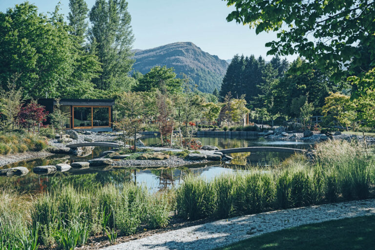 Wide view of Millbrook Mountain Garden with interconnected ponds, stepping stones, layered planting and a pavilion beneath the mountains.