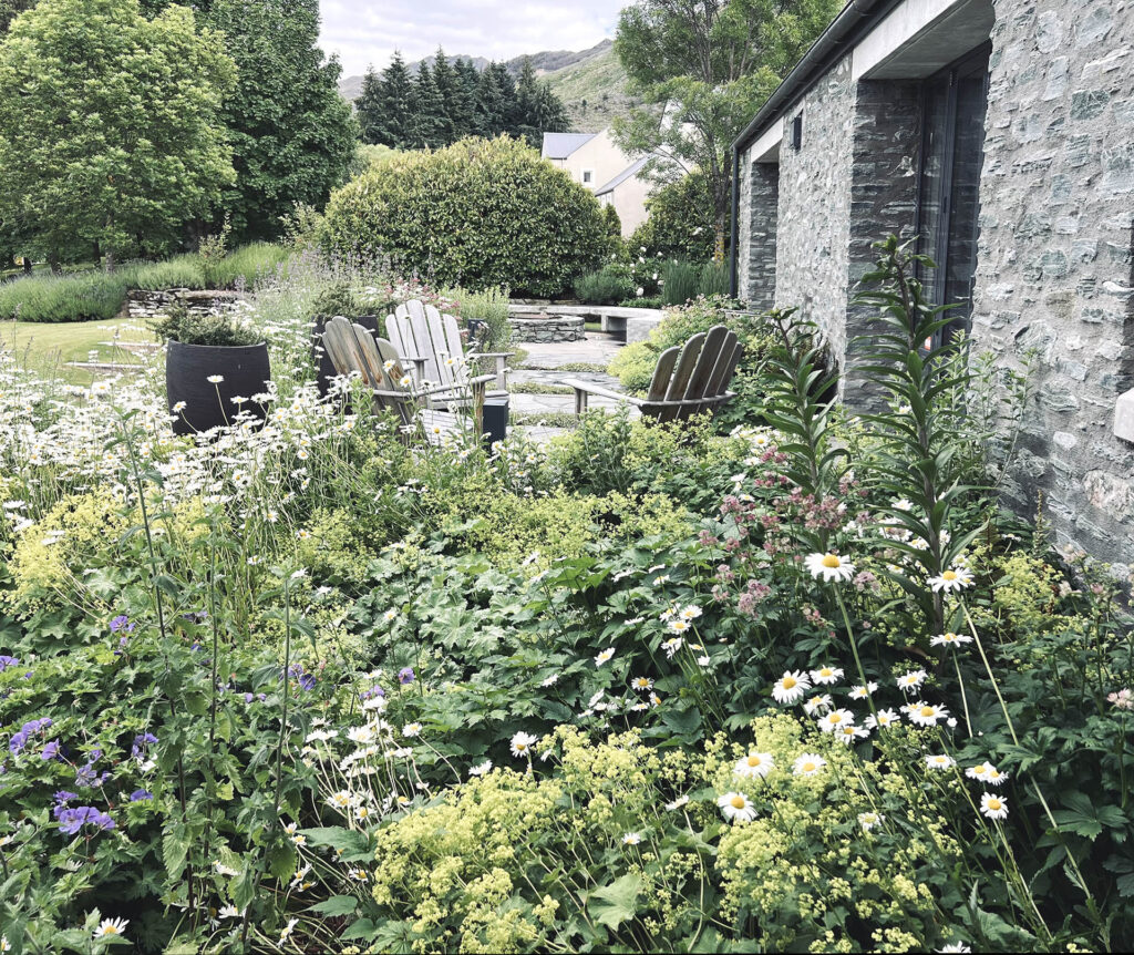 Layered perennial garden and outdoor seating beside the stone residence at Millbrook.