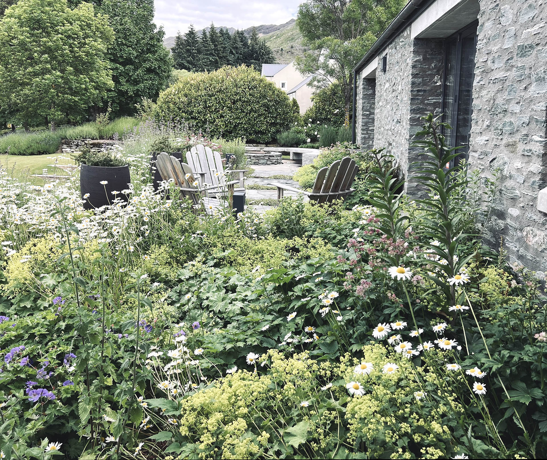 Layered perennial garden and outdoor seating beside the stone residence at Millbrook.
